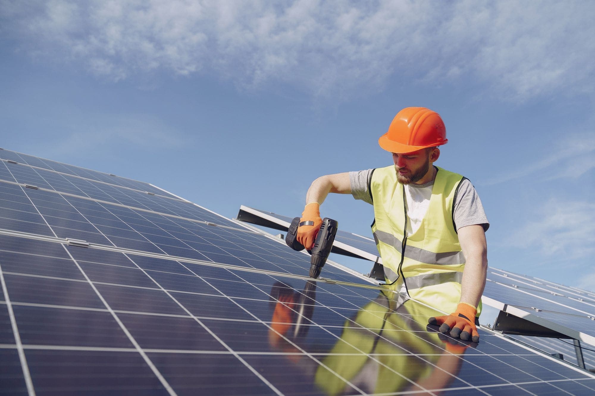 An accredited installer fitting solar panels under a clear sky